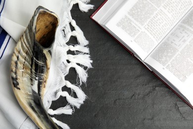 Photo of Tallit, shofar and open Torah on black table, flat lay. Rosh Hashanah celebration
