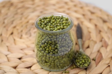 Photo of Glass jar of mung beans with spoon on wicker mat, closeup