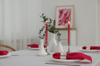 Beautiful table setting with green branches in vases and burning candles indoors. Stylish dining room