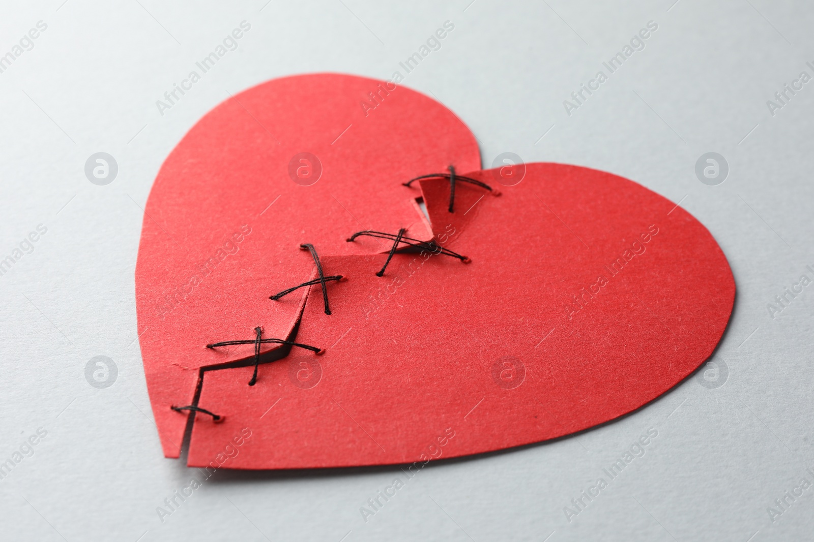 Photo of Broken heart. Torn red paper heart sewed with thread on light grey background, closeup