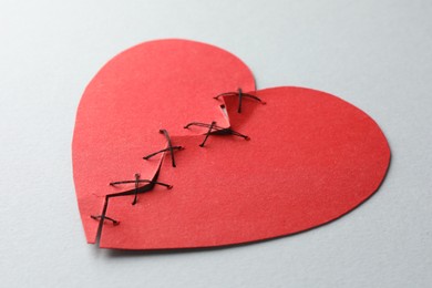 Broken heart. Torn red paper heart sewed with thread on light grey background, closeup