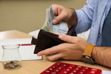 Man putting money into wallet at table indoors, closeup