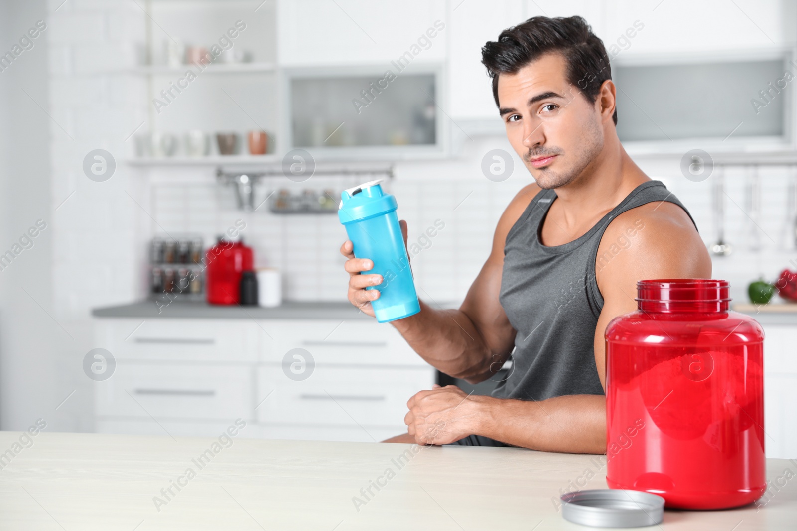 Photo of Young athletic man with protein shake powder in kitchen, space for text