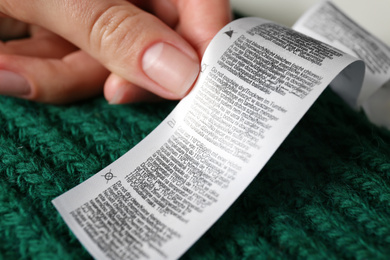 Photo of Woman reading clothing label with care instructions on dark knitted sweater, closeup