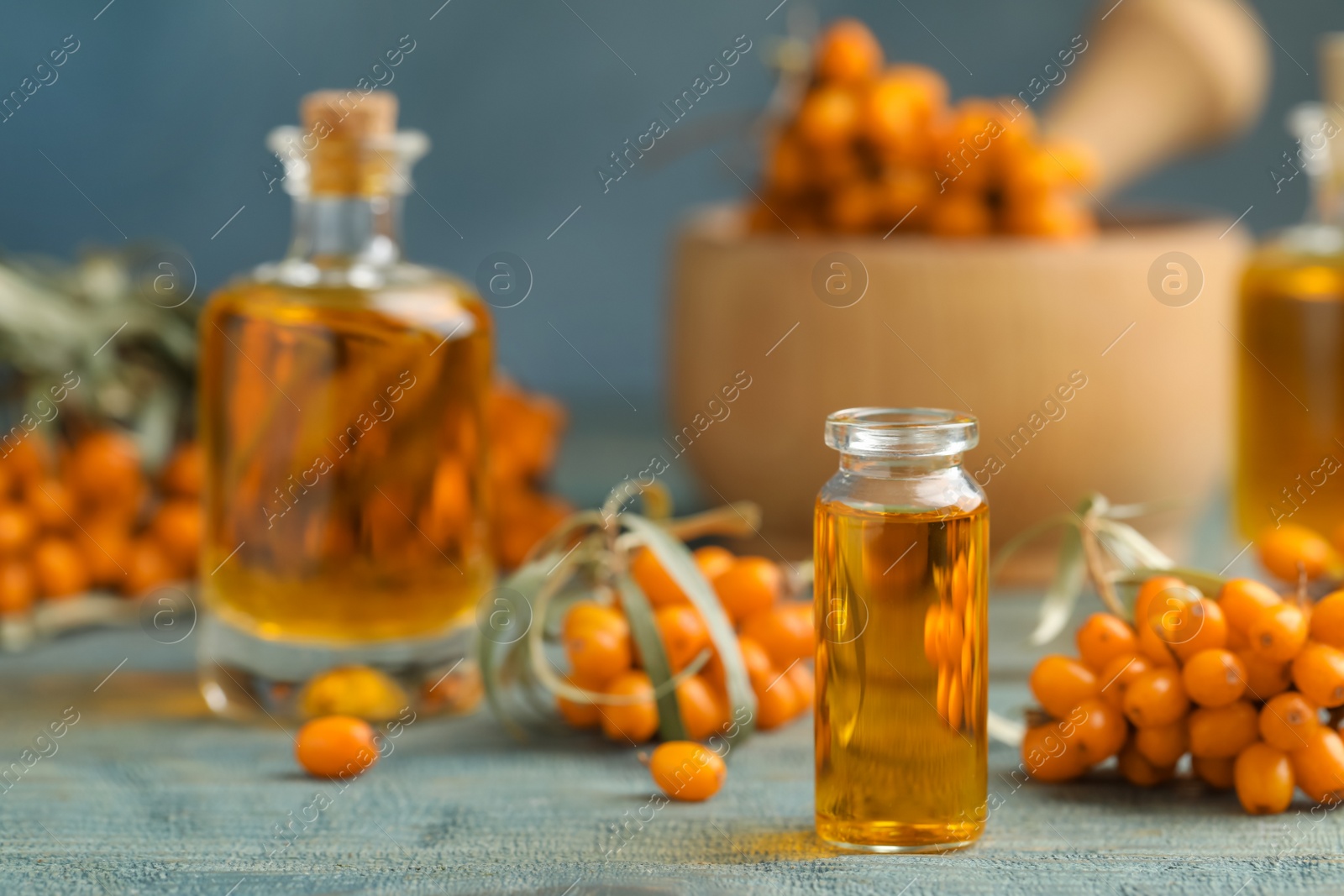 Photo of Natural sea buckthorn oil and fresh berries on blue wooden table. Space for text