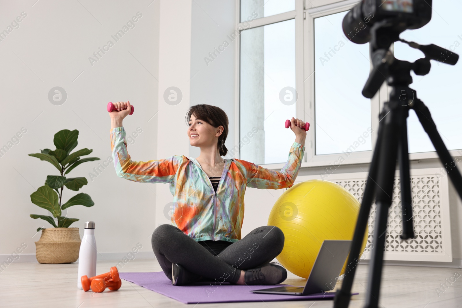 Photo of Happy sports blogger training with dumbbells while recording fitness lesson at home