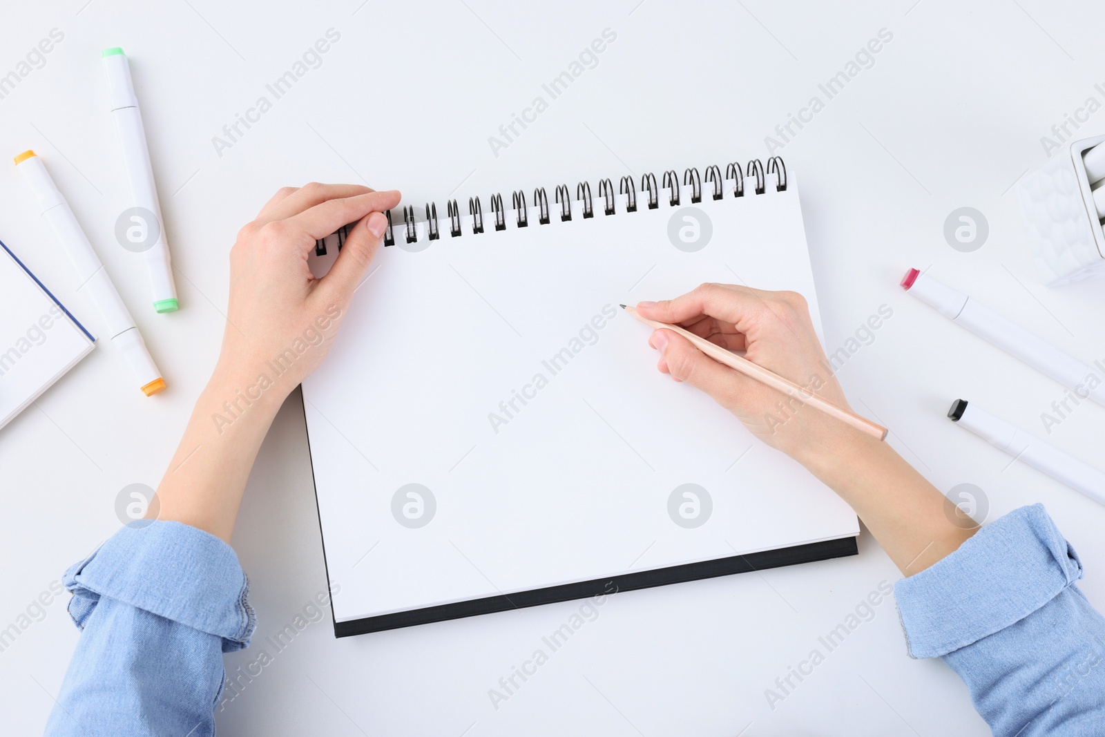 Photo of Young woman drawing in sketchbook at white table, top view