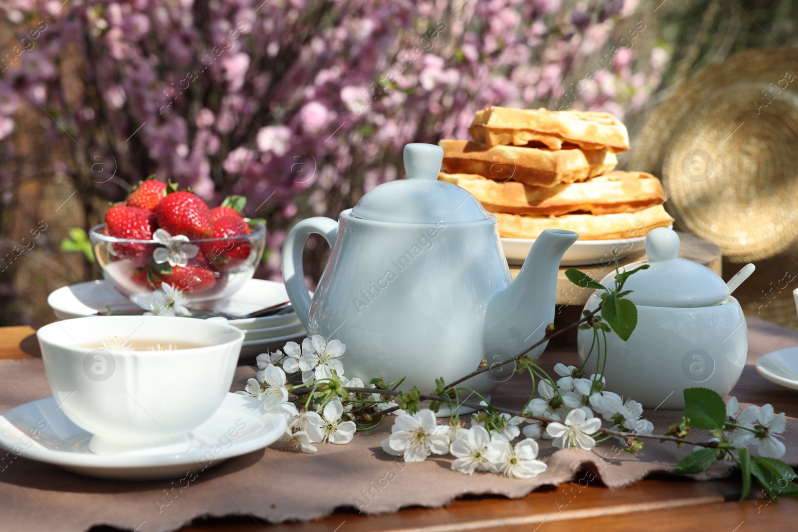 Photo of Beautiful spring flowers, freshly baked waffles and ripe strawberries on table served for tea drinking in garden