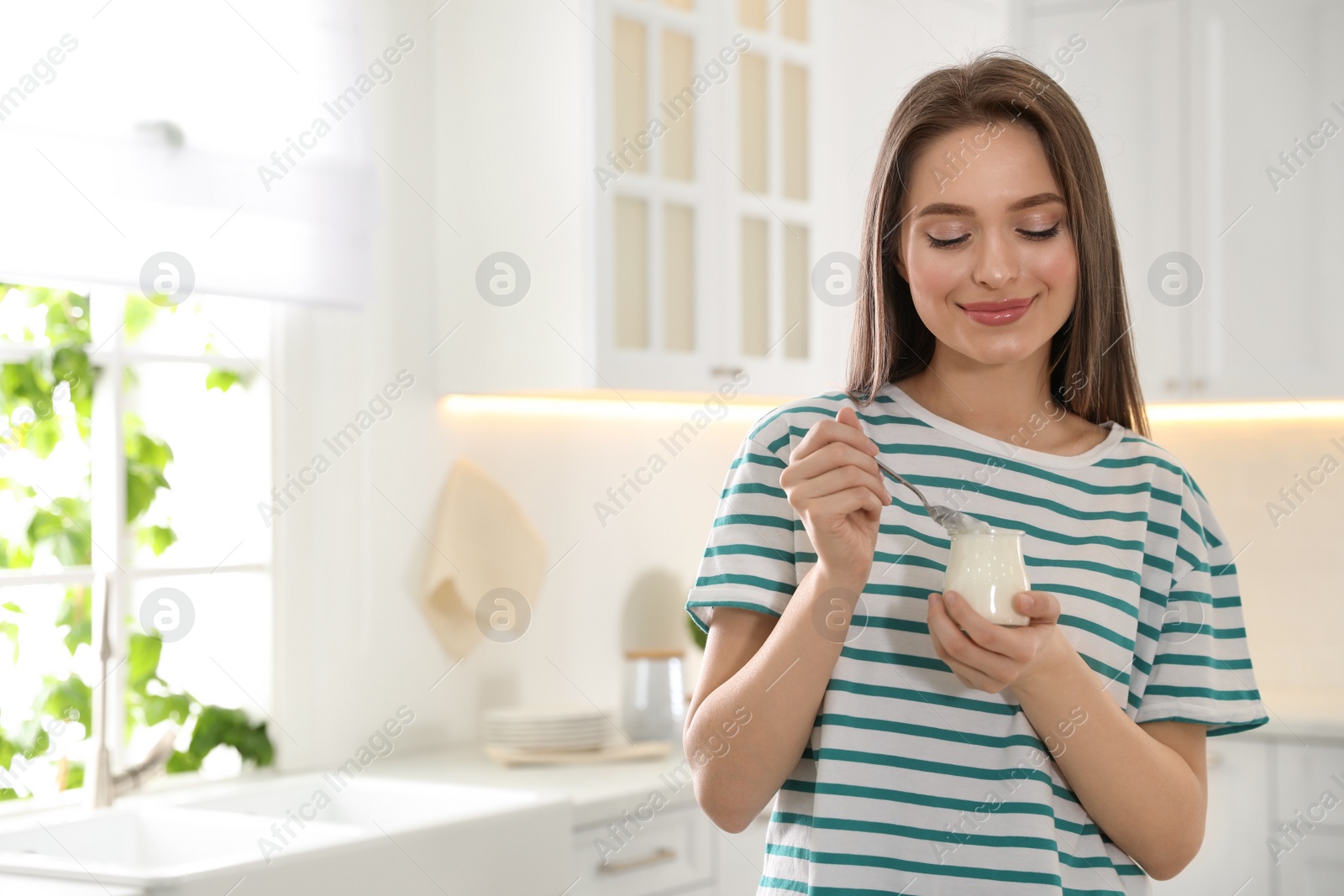 Photo of Young attractive woman with tasty yogurt in kitchen. Space for text