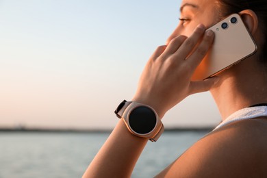 Woman with fitness tracker talking on phone near river, closeup. Space for text