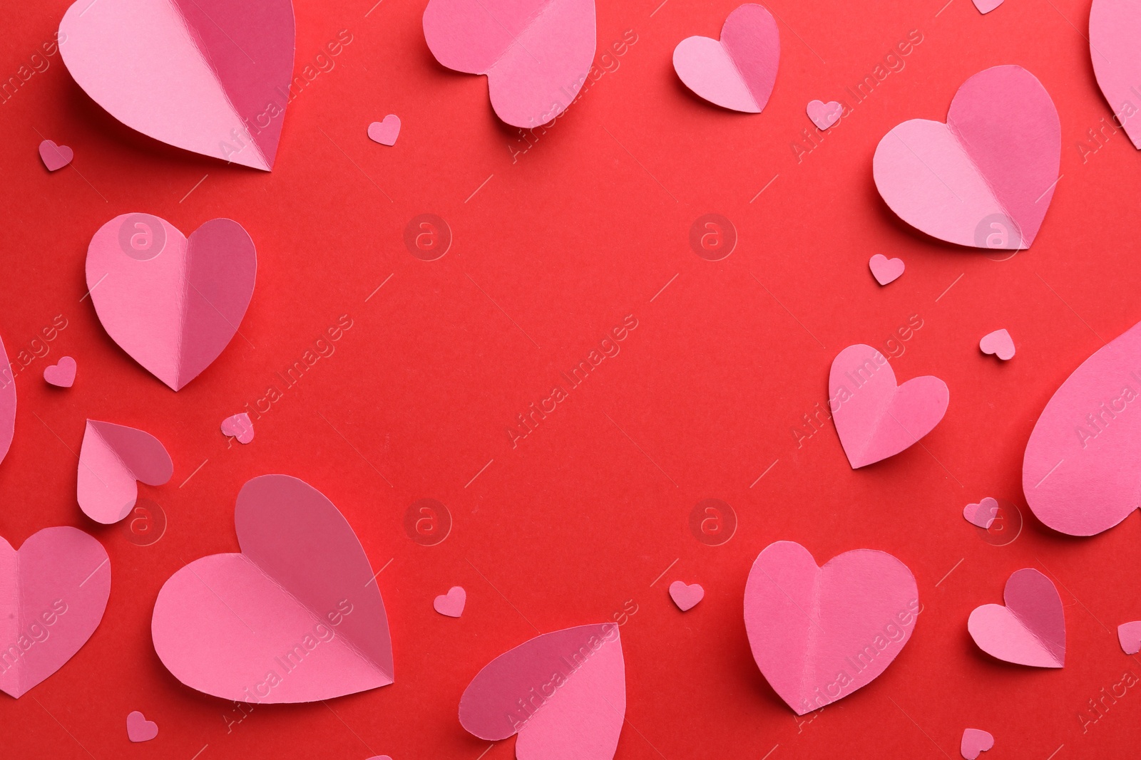 Photo of Frame of pink paper hearts on red background, flat lay. Space for text