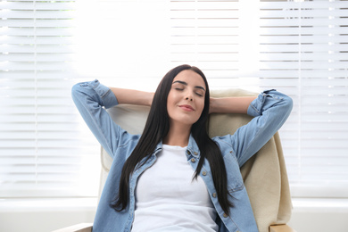 Young woman relaxing in armchair near window at home