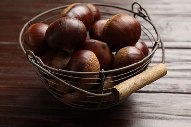 Photo of Sweet fresh edible chestnuts in metal basket on wooden table, closeup