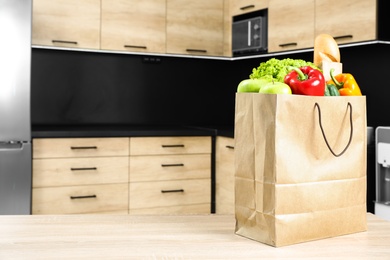 Paper bag with vegetables and other products on table in kitchen. Space for text