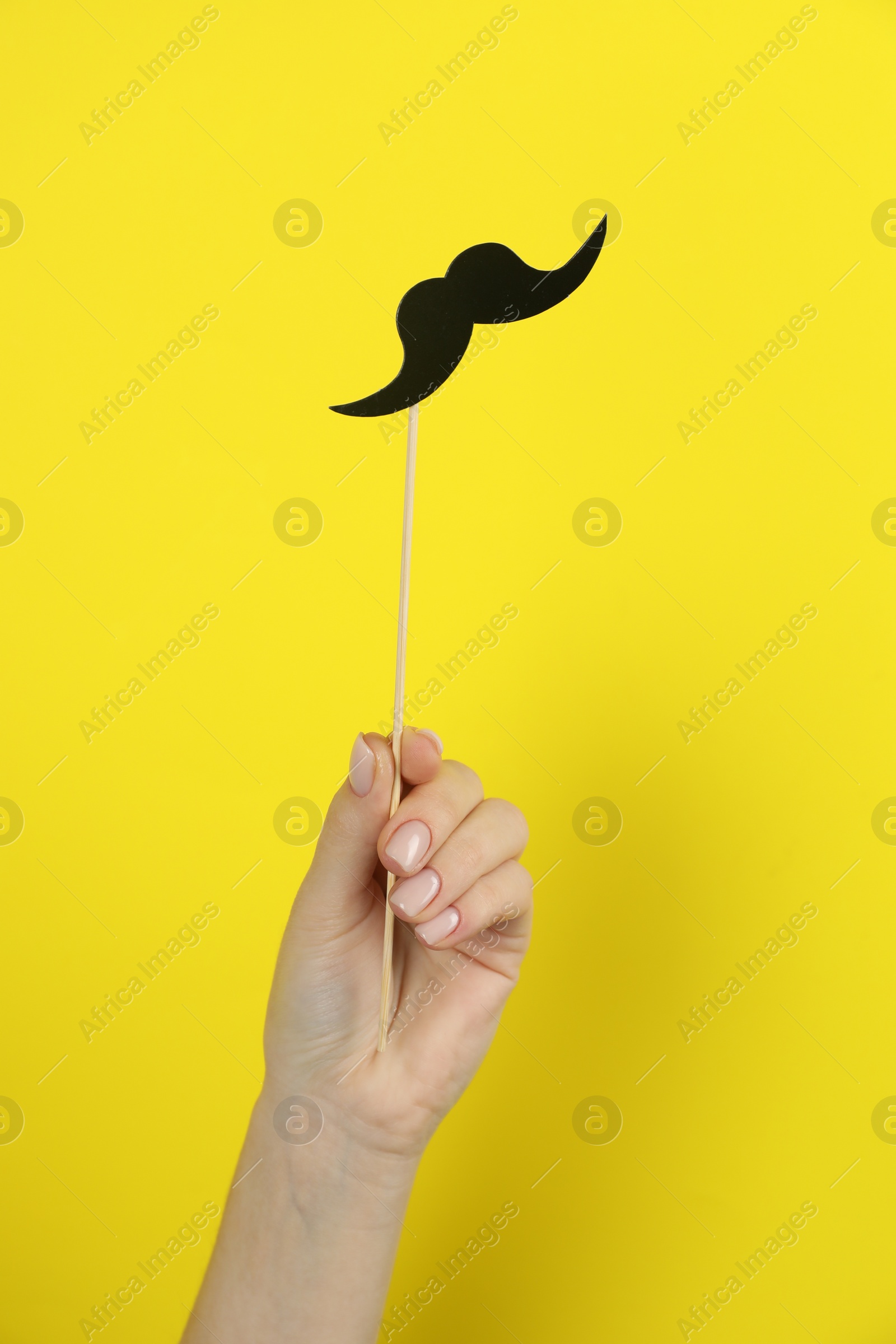 Photo of Woman with fake paper mustache on yellow background, closeup