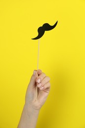 Woman with fake paper mustache on yellow background, closeup