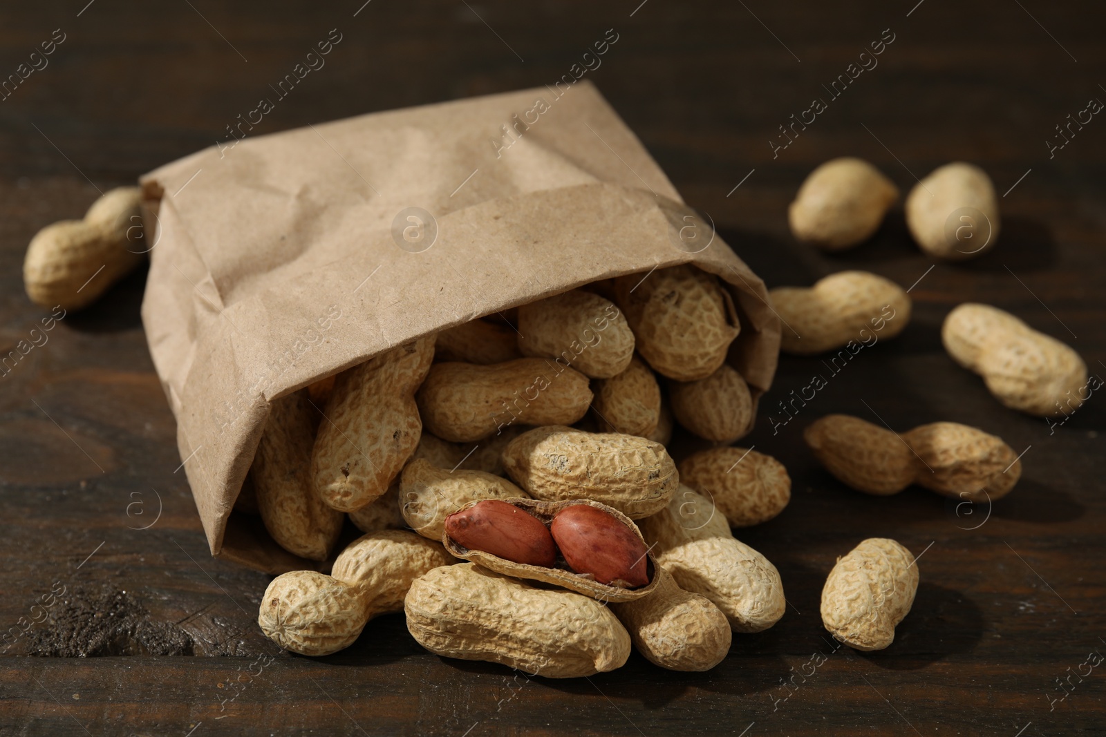 Photo of Paper bag with fresh unpeeled peanuts on wooden table, closeup