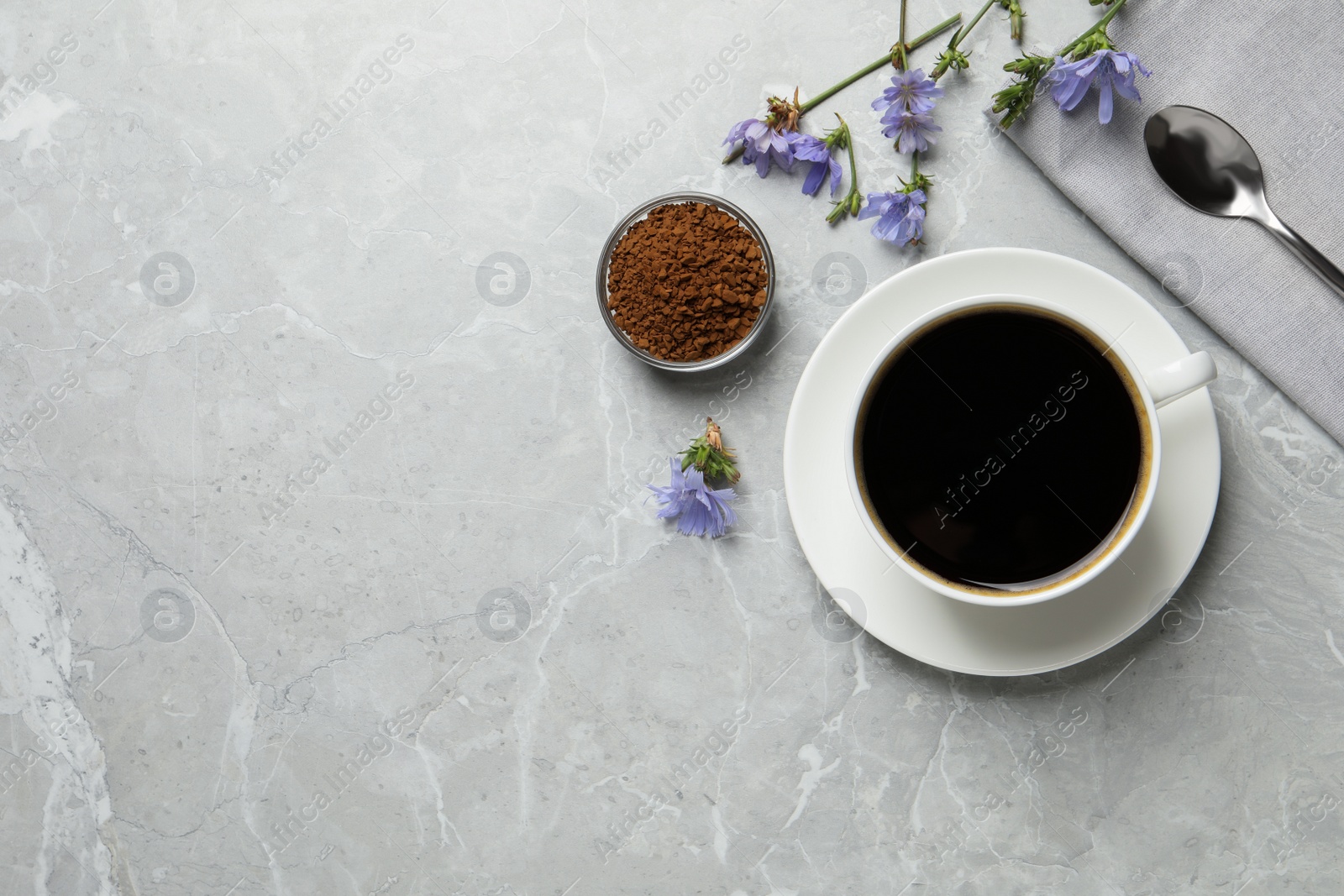 Photo of Cup of delicious chicory drink, granules and flowers on light grey marble table, flat lay. Space for text