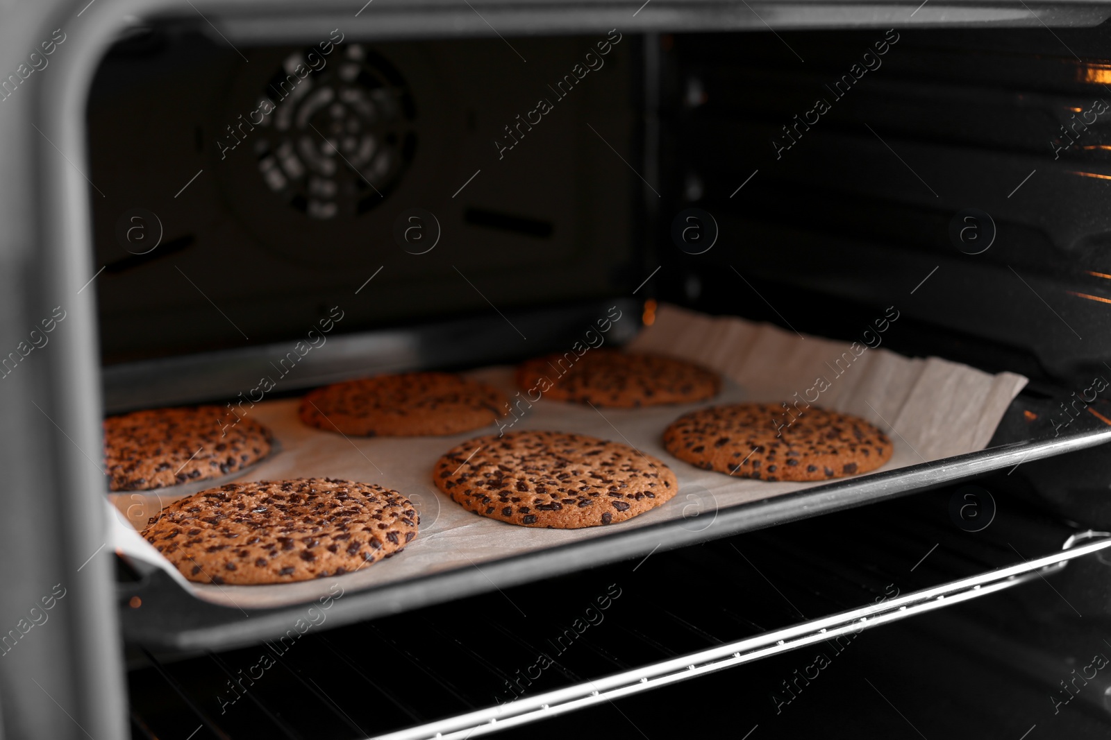 Photo of Open modern oven with freshly baked cookies on sheet, closeup