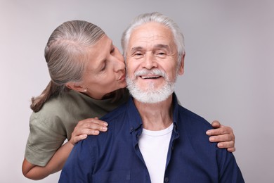 Photo of Senior woman kissing her beloved man on light grey background