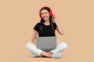 Photo of Happy woman with laptop listening to music in headphones on beige background