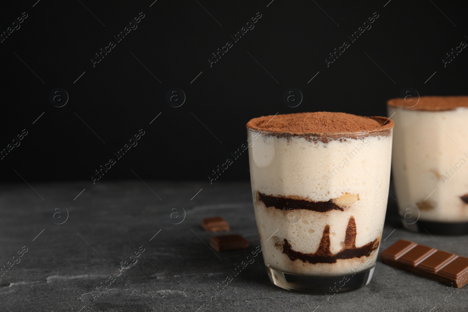 Photo of Two glasses of tiramisu cake on table against dark background, space for text