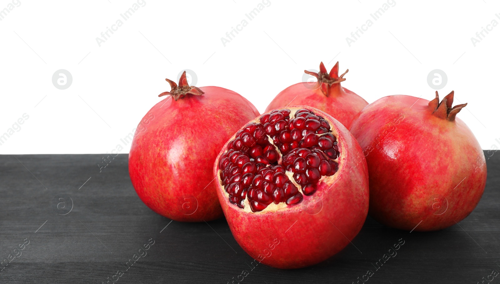 Photo of Fresh pomegranates on black wooden table against white background