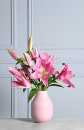 Photo of Beautiful pink lily flowers in vase on table against light wall