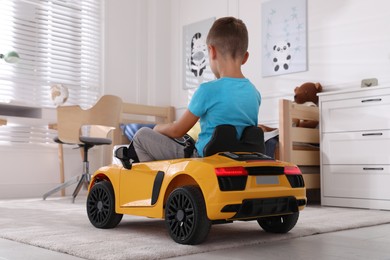 Photo of Cute little boy driving big toy car at home, back view