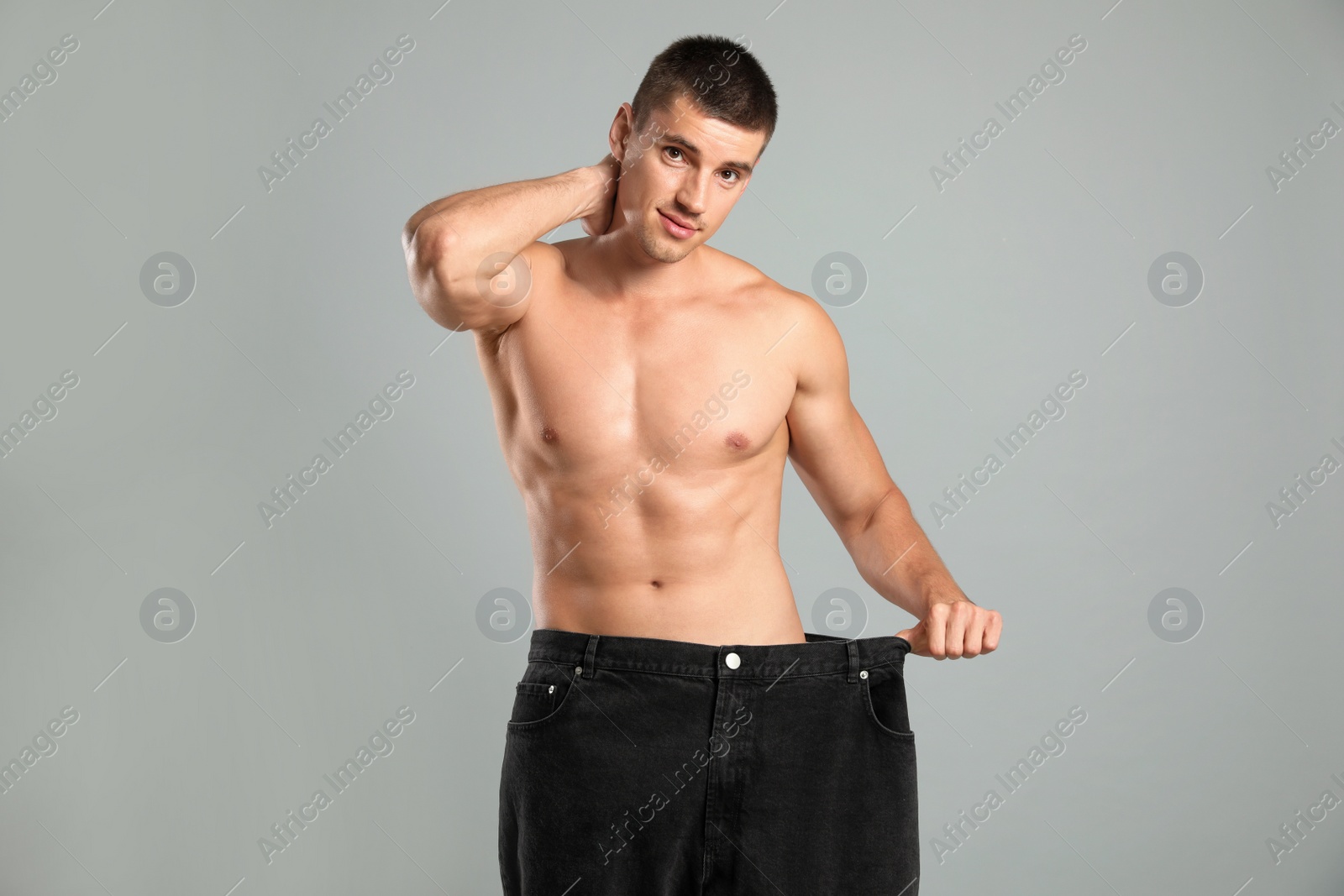 Photo of Young man with slim body in old big size jeans on grey background