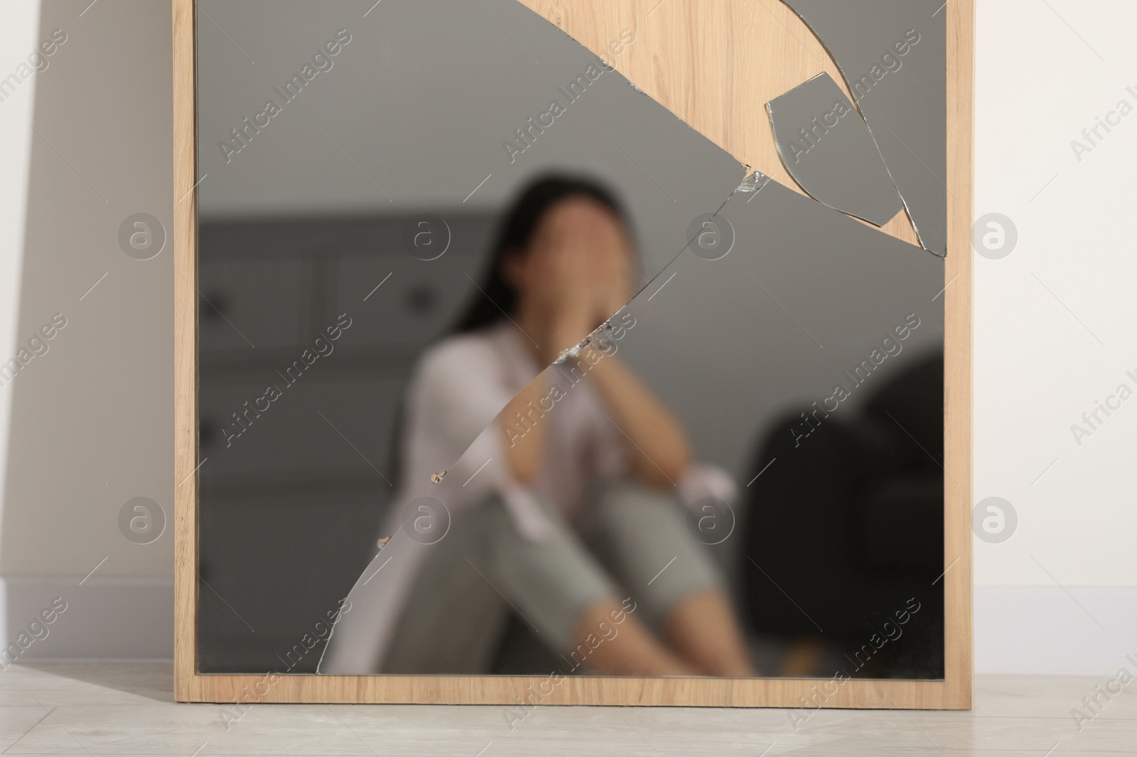 Photo of Mental problems. Blurred reflection of depressed woman in broken mirror indoors