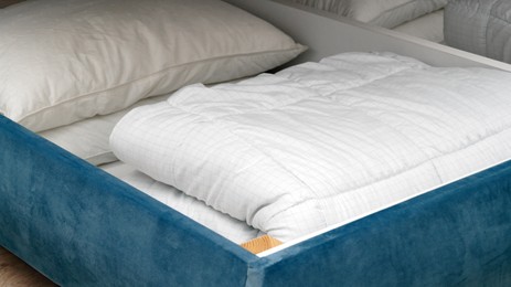 Photo of Storage drawer under bed with white blanket and pillows indoors, closeup