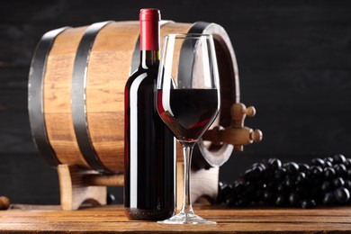 Photo of Delicious wine, wooden barrel and ripe grapes on table