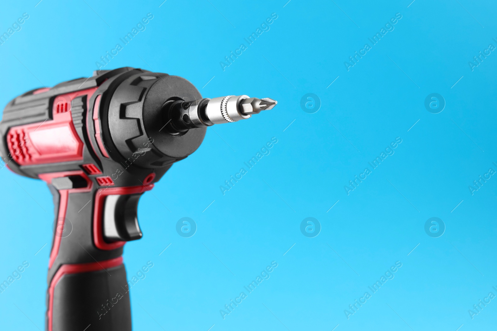 Photo of Modern electric screwdriver on light blue background, closeup. Space for text