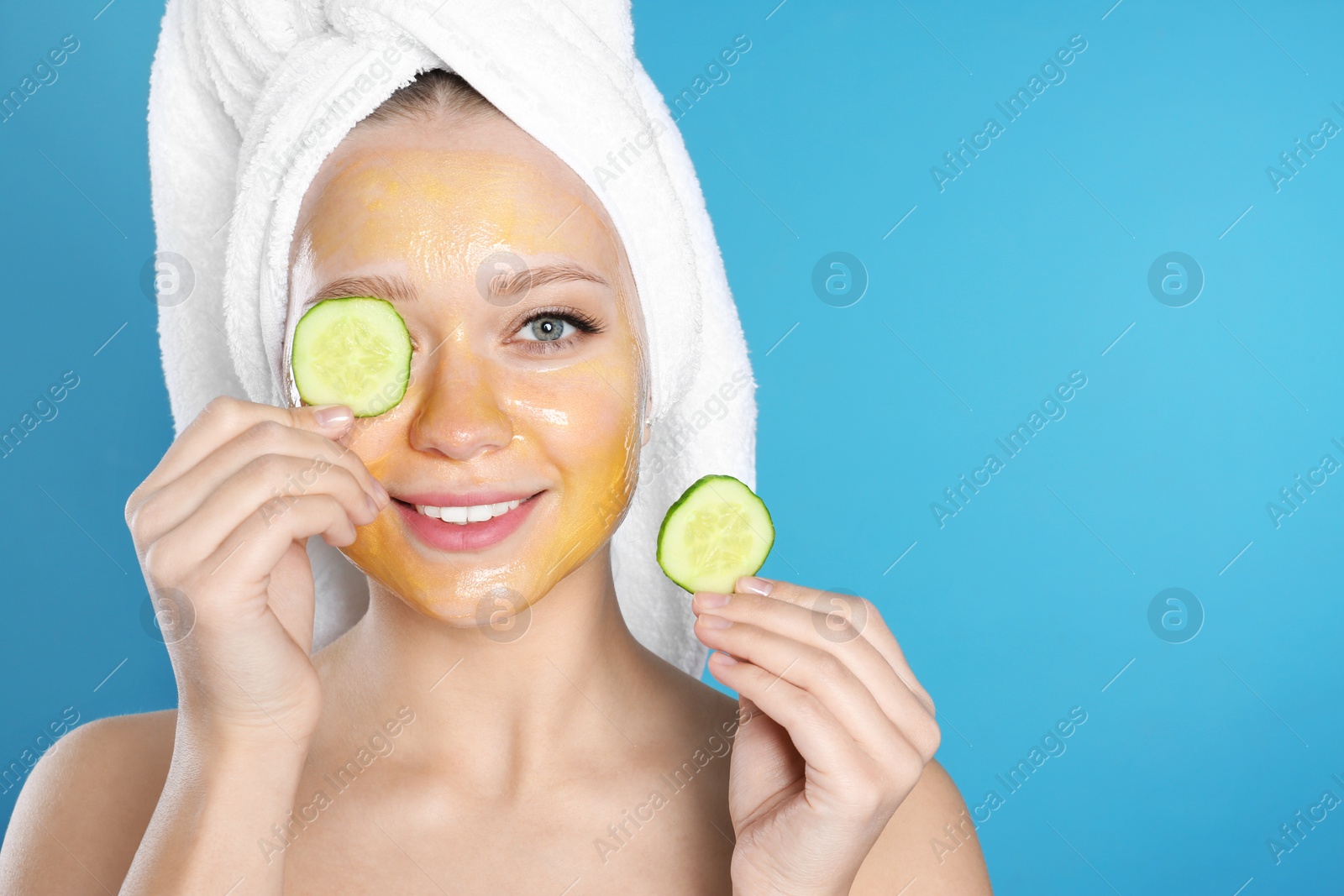 Photo of Beautiful woman holding cucumber slices near her face with natural mask against color background. Space for text