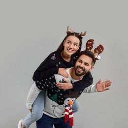 Photo of Happy young couple in Christmas sweaters and reindeer headbands on grey background. Space for text