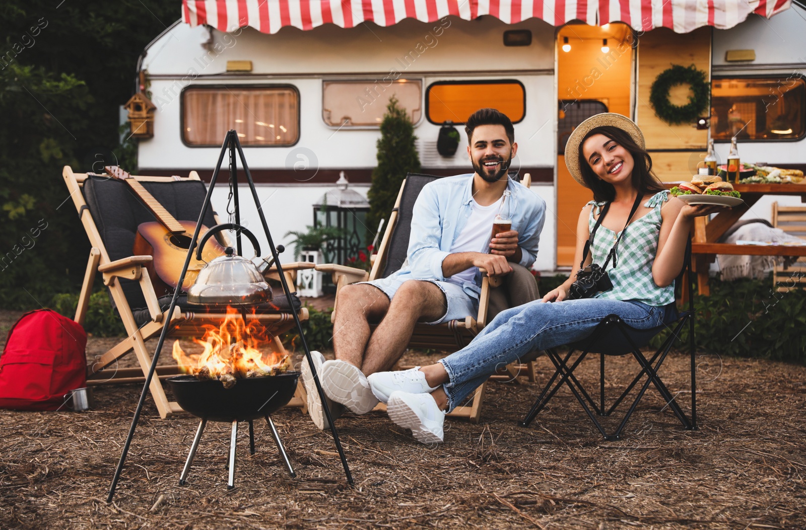 Image of Happy couple resting near trailer. Camping season