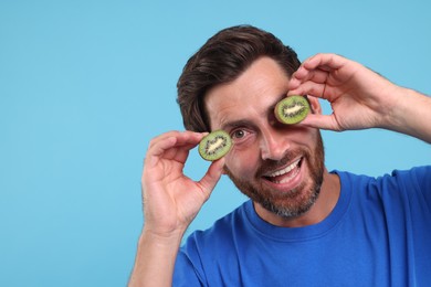 Man holding halves of kiwi on light blue background, space for text