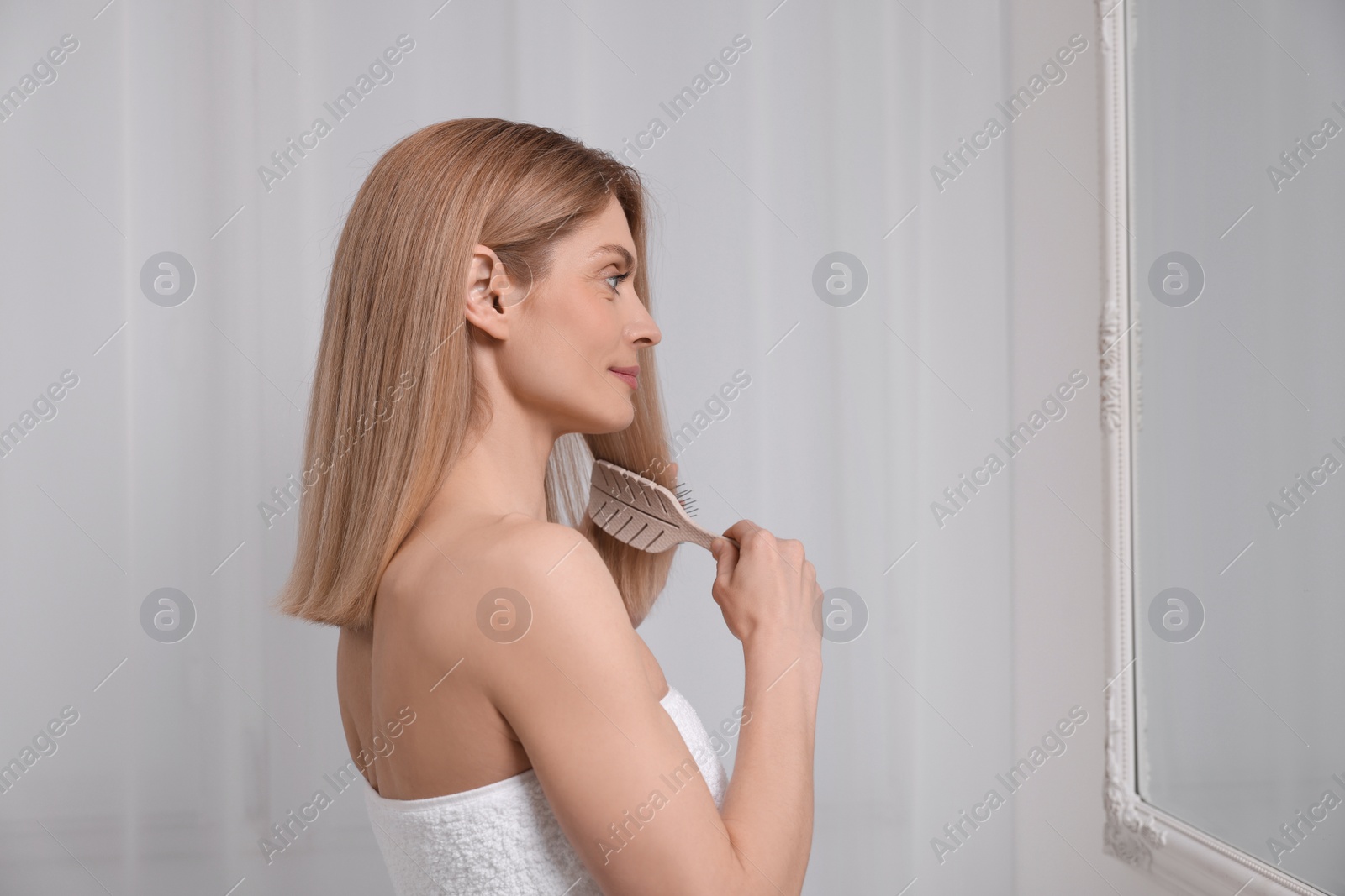 Photo of Beautiful woman brushing her hair near mirror in room