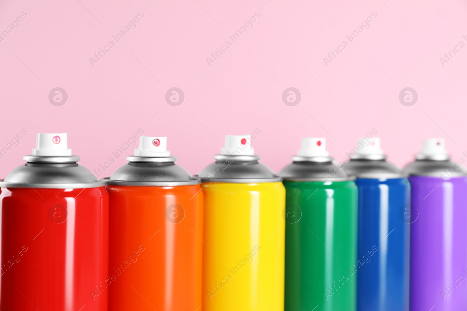 Photo of Colorful cans of spray paints on pink background, closeup
