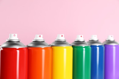 Colorful cans of spray paints on pink background, closeup