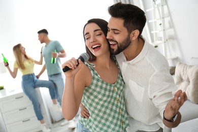 Photo of Happy couple singing karaoke with friends at home