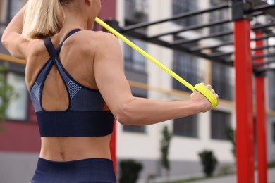 Woman doing exercise with fitness elastic band at outdoor gym, closeup