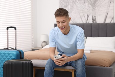 Smiling guest with smartphone and suitcase in stylish hotel room