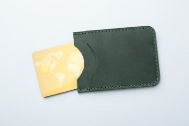 Woman holding leather card holder with credit card on light grey background, top view