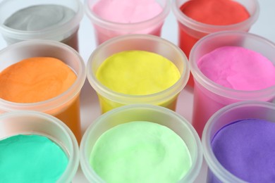 Plastic containers with colorful play dough on white background, closeup