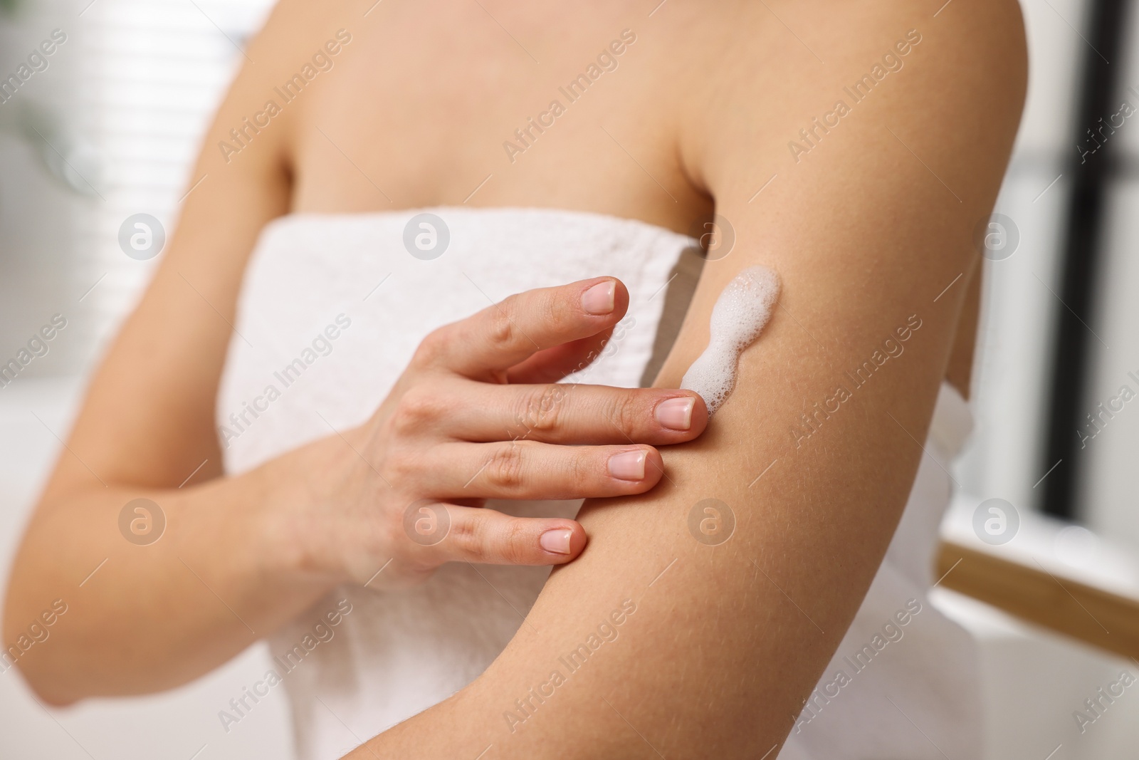 Photo of Woman applying self-tanning product onto arm indoors, closeup