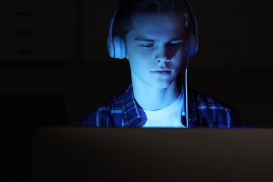 Photo of Teenage boy in headphones using computer at night. Internet addiction