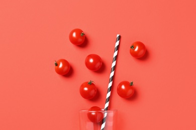 Cherry tomatoes, straw and glass on coral background, flat lay