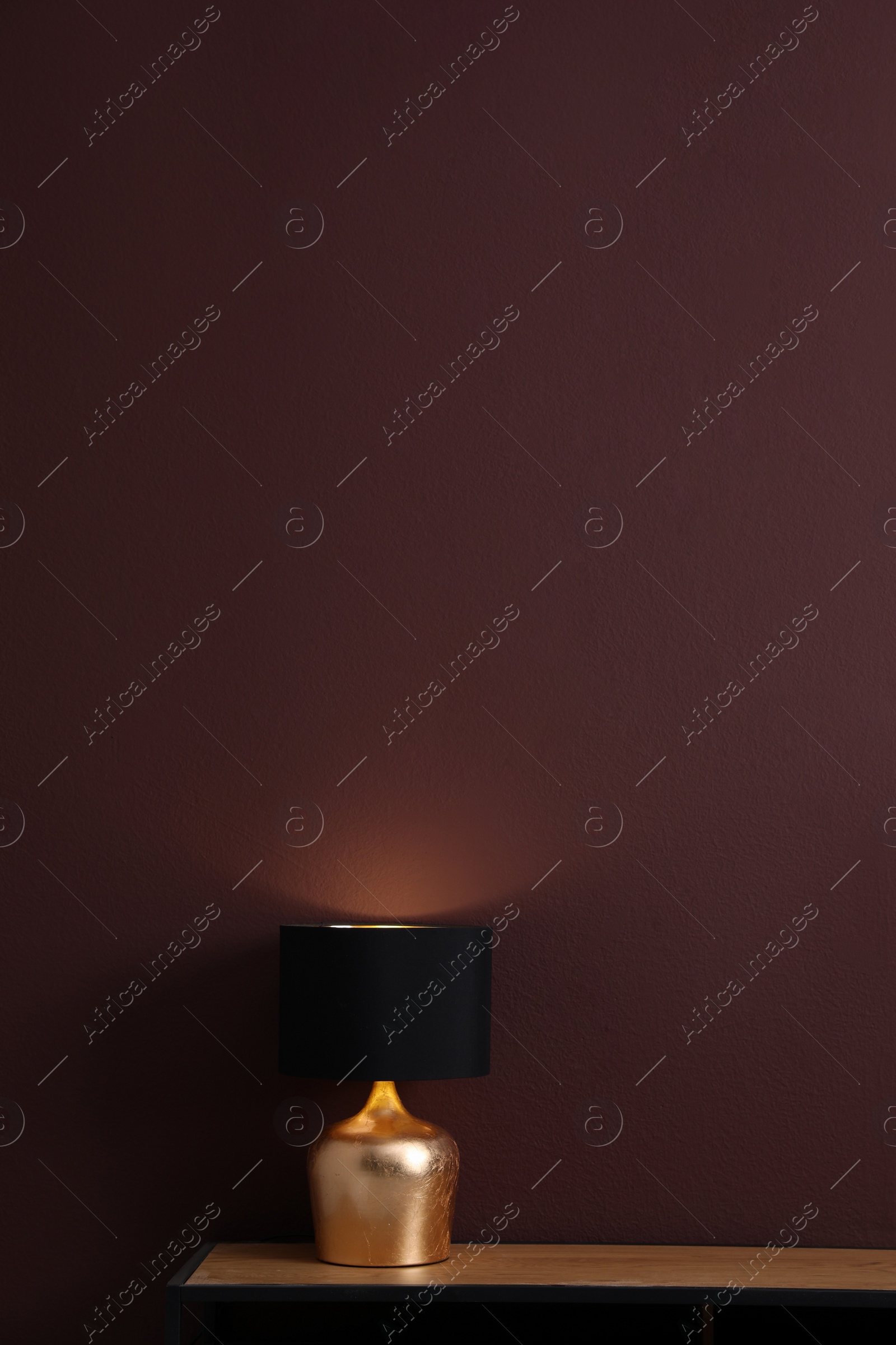 Photo of Wooden table with lamp near brown wall in room, space for text